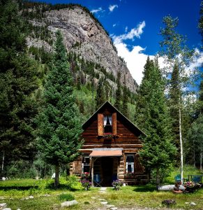 log cabin in front of steep mountain face in colorado summer